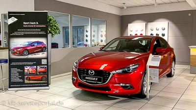 Ein Neuwagen steht in einem Autohaus in einem Verkaufsraum. Eine große Info- und Preistafel zeigt die Ausstattung und die Preise.