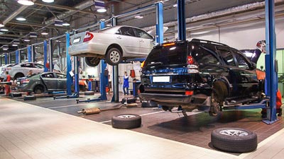 In einer großen Werkstatt sind Autos auf den Hebebühnen und werden bearbeitet und gewartet.